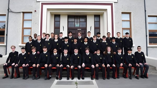 Un grupo de estudiantes del De la Salle College Churchtown está en uniforme escolar formal frente a un magnífico edificio.
