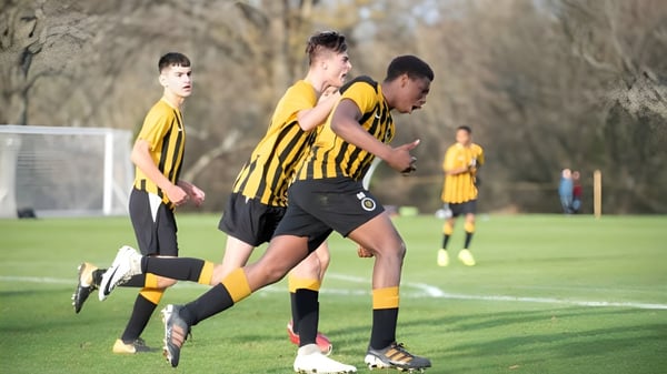 Estudiantes del De la Salle College (Macroom) juegan al fútbol en un campo de juego con una portería visible.