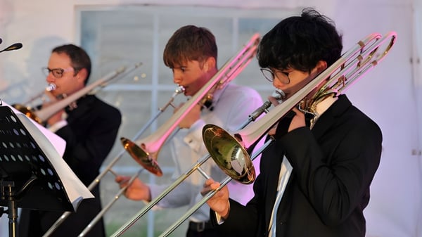 Estudiantes de la Dean Close School tocan varios instrumentos de metal en un escenario durante una actuación.