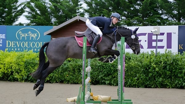 Una estudiante de la Dean Close School monta en una competencia de salto ecuestre frente a árboles verdes.