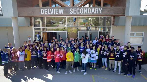 Un gran grupo de estudiantes y personal se reúne frente al edificio de la Delview Secondary School.