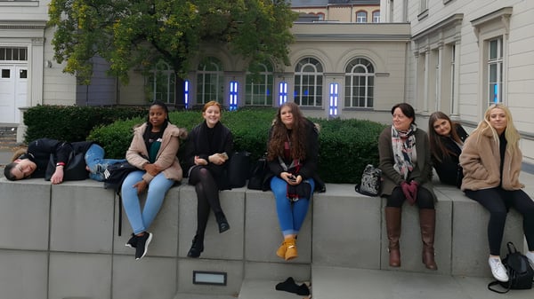Un grupo de alumnas está sentada frente a un edificio con ventanas de arco en un muro de piedra en el terreno de la Denefield School.