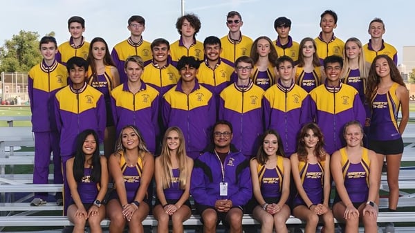 Un grupo de jóvenes atletas en uniformes amarillo-púrpura posan en el campo deportivo del Denver Public School District con un estadio al fondo.