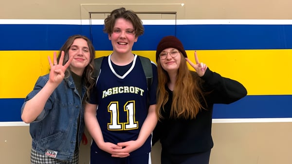 Tres estudiantes de Desert Sands Schools posan frente a un fondo azul y amarillo con diferentes gestos de las manos.