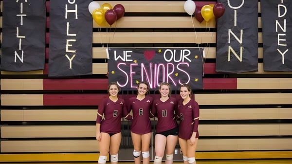 Cuatro estudiantes de la Dexter High School están en uniformes idénticos frente a un cartel con la inscripción We love our seniors.