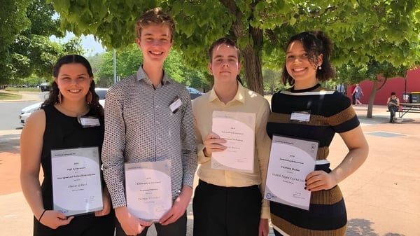 Cuatro estudiantes del Dickson College están sonriendo en el parque con árboles y áreas verdes de fondo.