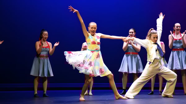 Un grupo de bailarinas presenta en el escenario de la Diocesan School For Girls una colorida actuación de baile frente a un fondo azul.