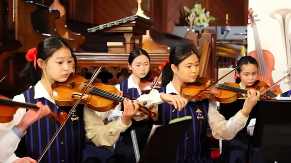 Alumnas de la Diocesan School For Girls tocan violines juntas en una sala de música.