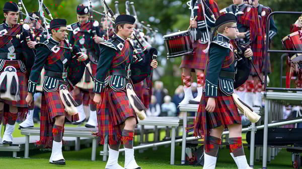 Un grupo de hombres en faldas escocesas y uniformes tocan gaitas y tambores en un desfile en la Dollar Academy.