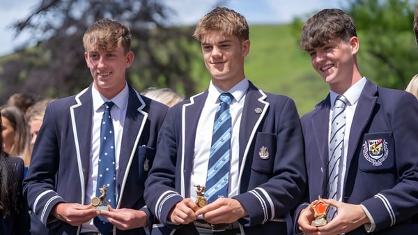 Tres estudiantes de la Dollar Academy están juntos en un campo con árboles de fondo.