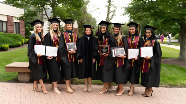 Un grupo de graduadas y graduados del Dominican College Galway está al aire libre en un camino pavimentado rodeado de vegetación verde.