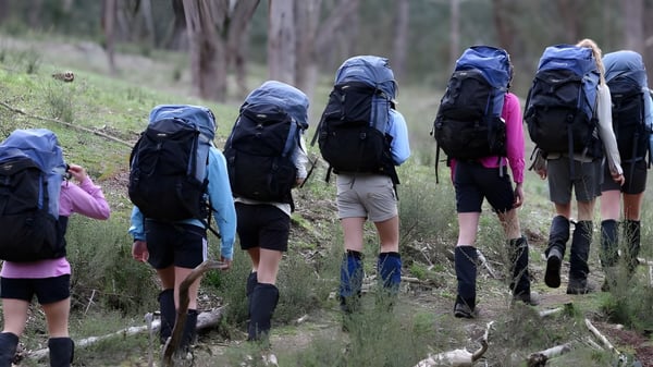 Un grupo de estudiantes del Dominican College Galway camina con grandes mochilas por un sendero forestal.