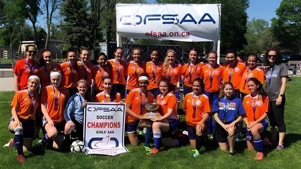 Un grupo de estudiantes de la Donald A. Wilson School posan frente a un banner de FSSAA en el campo de fútbol.