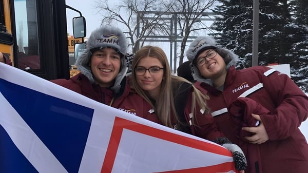 Tres estudiantes de Dorset Collegiate llevan sudaderas rojas idénticas y sostienen juntas un gran banner.
