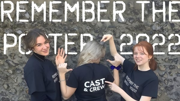 Tres estudiantes del Dover College posan frente a una pared con graffiti y la inscripción 'Remember the Poster 2022'.