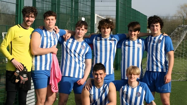 Un grupo de jóvenes futbolistas está frente a una cerca de alambre verde en el terreno de D'Overbroeck's College.