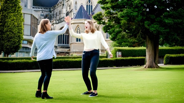 Dos estudiantes están de pie en una pradera frente a un edificio histórico en el terreno de la Downside School.