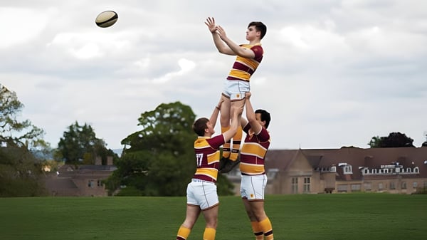 Dos estudiantes de la Downside School juegan al rugby en un campo deportivo con árboles de fondo.