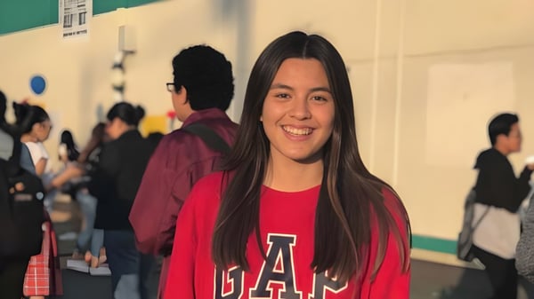 Una estudiante sonriente con una camiseta roja de GAP está frente a un grupo de personas en el campus de la Downtown Magnet High School.