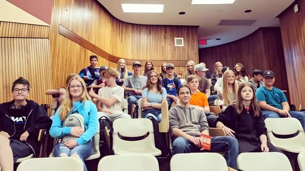 Un grupo de estudiantes está sentado en la sala revestida de madera en el campus de la Dr. Elliott School.