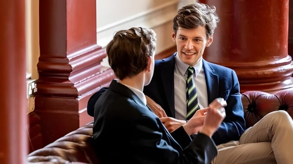 Dos personas mantienen una conversación en un ambiente formal en el campus del Dulwich College.