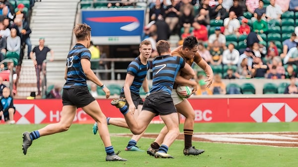Un grupo de jugadores de rugby del Dulwich College lleva camisetas azules y blancas y juega un partido en un campo de césped.