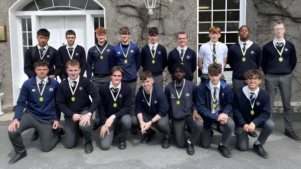 Un grupo de alumnos de la Dundalk Grammar School está frente a un edificio con fachada de piedra y ventanas de arco.