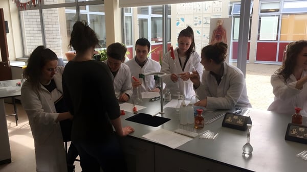 Estudiantes del Dungarvan College están en batas de laboratorio blancas alrededor de una mesa en el laboratorio.
