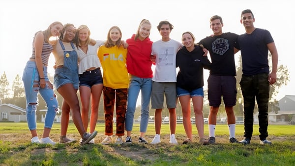Un grupo de estudiantes de la Dunn School está de pie juntos en un campo con casas de fondo.