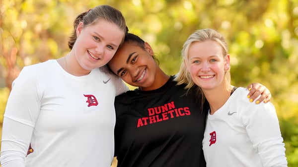 Tres estudiantes femeninas de la Dunn School posan afuera en ropa deportiva frente a un fondo natural.