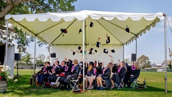 Estudiantes de la Dunn School están sentados durante la ceremonia de graduación al aire libre bajo una gran carpa blanca.