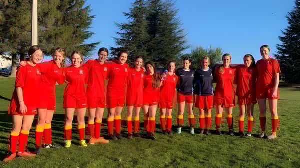 Un grupo de jóvenes futbolistas en camiseta roja está en un campo deportivo de la Dunstan High School.
