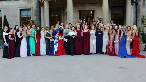 Un gran grupo de mujeres en vestidos de gala está de pie frente a un magnífico edificio en el terreno de la Durham School.