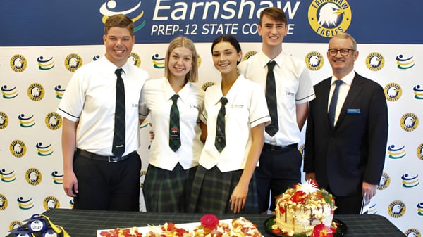 Un grupo de estudiantes posa frente a un fondo con el logo del Earnshaw State College.