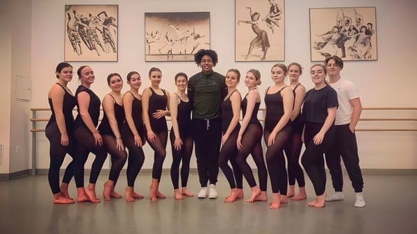 Un grupo de baile de estudiantes en el estudio del East Sussex College Eastbourne se agrupa frente a una decoración de pared relacionada con el baile.