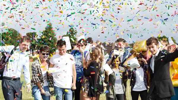 Estudiantes del East Sussex College Eastbourne celebran al aire libre bajo colorido confeti con árboles de fondo.