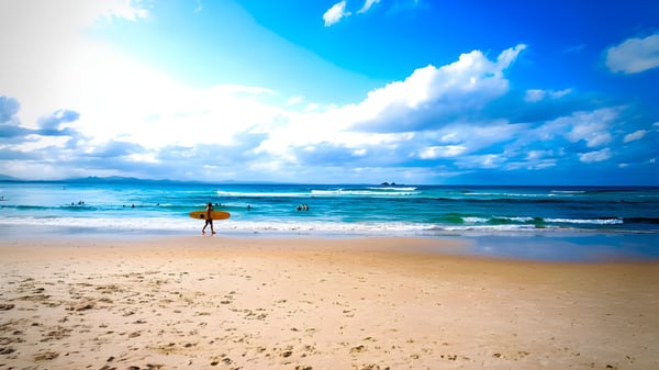 Un surfista camina por la playa soleada bajo un cielo azul en el terreno de la Eastern Fleurieu R-12 School.