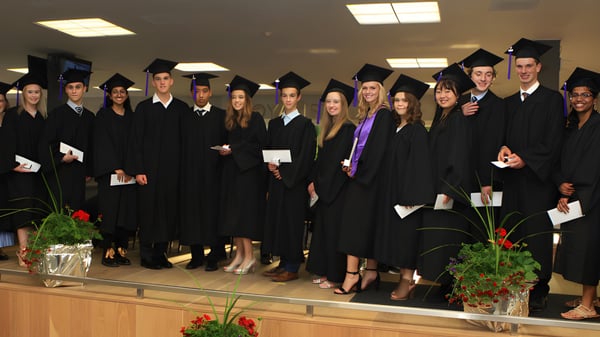 Un grupo de graduados de la Eastside Secondary School se encuentra en una sala con plantas y iluminación.
