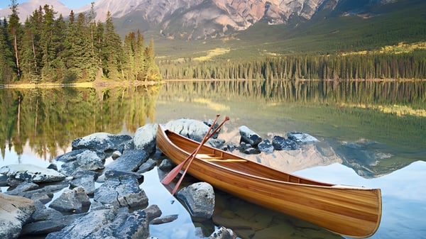 Una canoa de madera yace en la orilla rocosa de un lago tranquilo con montañas y bosques en los alrededores de la Eastside Secondary School.