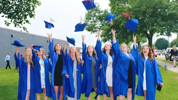 Un grupo de graduados lanza sus birretes azules al aire en el campus de la Eastview Secondary School.
