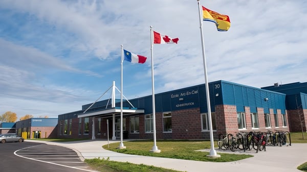 El edificio de École Arc-en-ciel muestra la bandera canadiense y la bandera española frente a la entrada principal con aparcamientos para bicicletas delante.