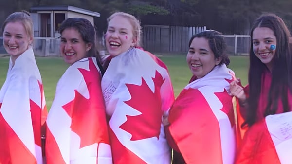 Un grupo de estudiantes de École Arc-en-ciel está en un campo y sostiene banderas canadienses.