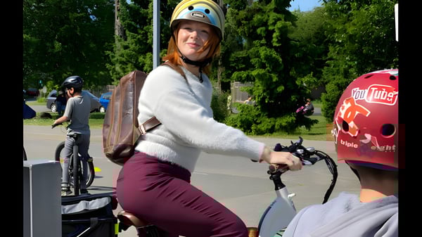 Una estudiante de la École Au-coeur-de-l'île monta en bicicleta con casco en un carril bici rodeado de árboles y otros ciclistas.
