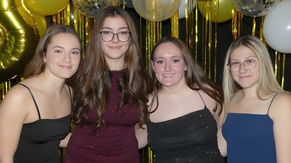 Cuatro alumnas vestidas formalmente posan frente a globos dorados y plateados en el campus de la École Clément-Cormier.