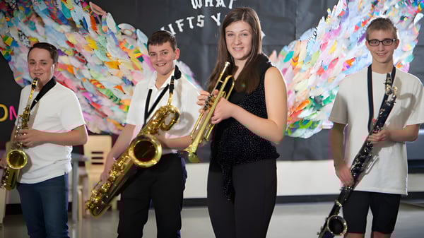Un grupo de músicos está frente a un colorido fondo abstracto en el campus de la École Dansereau Meadows School.
