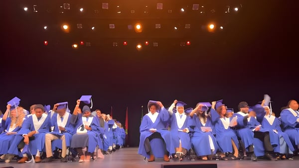 Un grupo de graduados de la École secondaire publique Gisèle-Lalonde está en togas azules en un escenario con un fondo iluminado.
