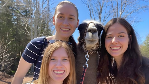 Tres mujeres sonrientes posan con un gran perro en el bosque en el terreno de la École L’Odyssée.