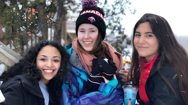 Tres estudiantes de la École Sainte-Anne posan juntas afuera frente a un bosque nevado.