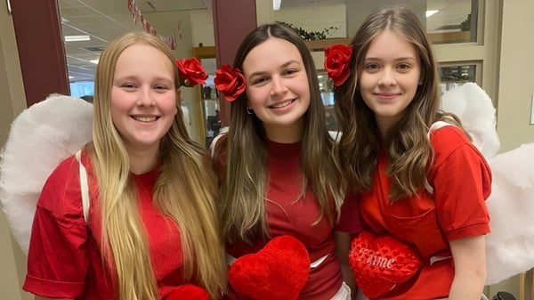 Tres estudiantes de la École secondaire Népisiguit llevan camisetas rojas con motivos de corazón y sonríen en un entorno interior.
