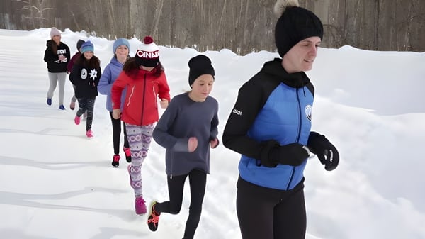 Estudiantes de la École Sophie Morigeau caminan con ropa de invierno abrigada a través de un bosque nevado con árboles sin hojas.
